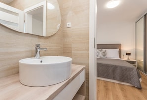 Ein modernes Badezimmer mit einem runden Waschbecken und einem großen Spiegel. Das Badezimmer verfügt über einen Holzboden und sandfarbene Wände.