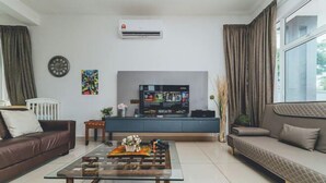 A modern living room with a sofa, a coffee table, a TV, and an air conditioning unit. - d'Lux 6BR16-25px Pool/BBQ/NetFlx/HotPot/KTV/Mahjong (Bandar Penawar)