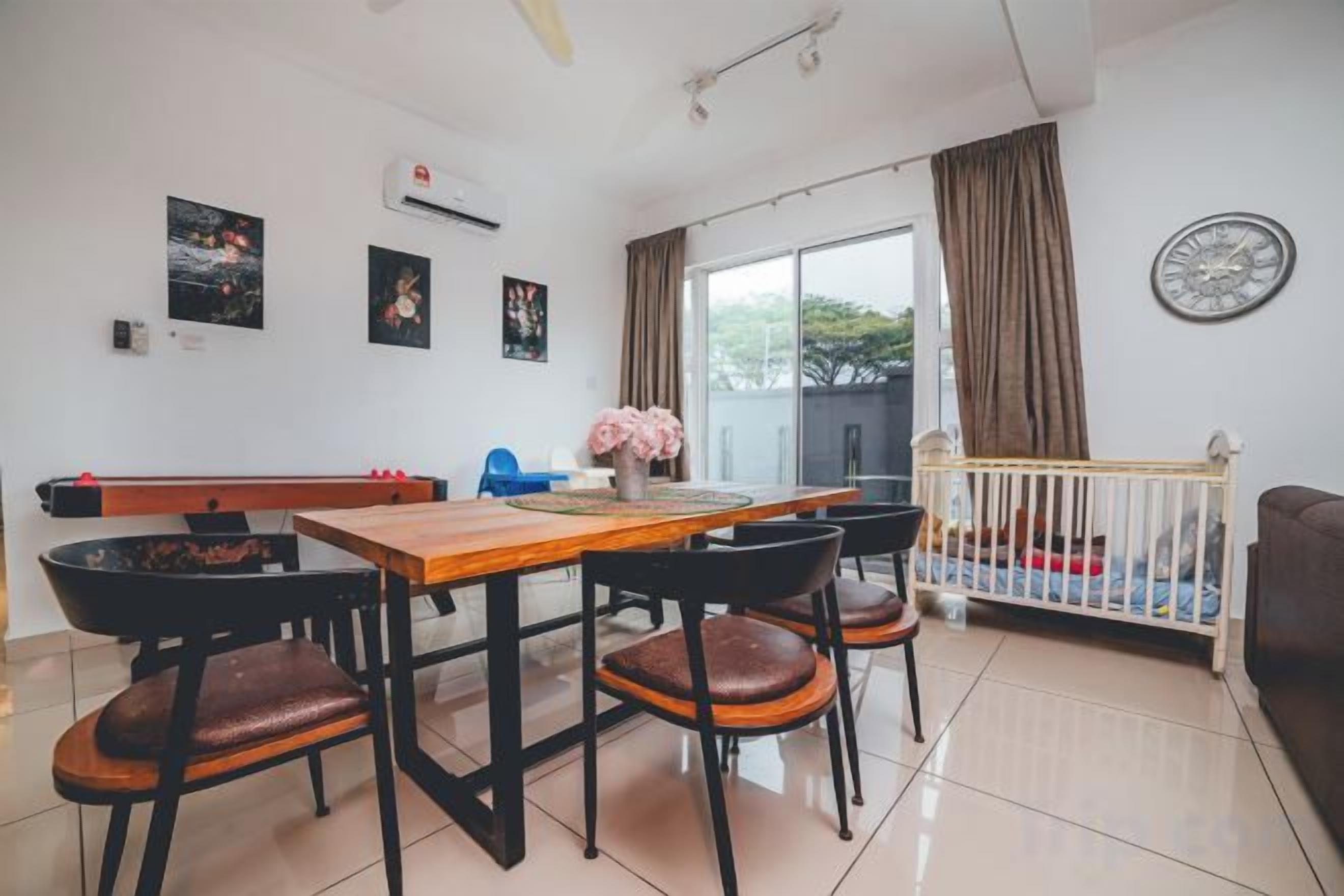 Uma sala de jantar com mesa e cadeiras de madeira, um berço e vista para o exterior.
