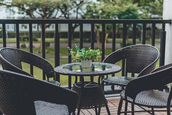 A balcony with wicker chairs and a table, a potted plant, and a view of a garden.