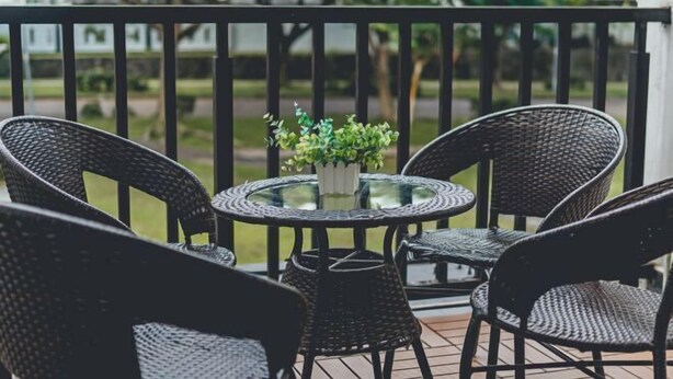 A balcony with wicker chairs and a glass table, a small potted plant, and a view of a park. - d'Lux 6BR16-25px Pool/BBQ/NetFlx/HotPot/KTV/Mahjong (Bandar Penawar)
