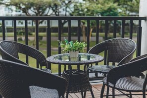 A balcony with wicker chairs and a glass table, a small potted plant, and a view of a park. - d'Lux 6BR16-25px Pool/BBQ/NetFlx/HotPot/KTV/Mahjong (Bandar Penawar)