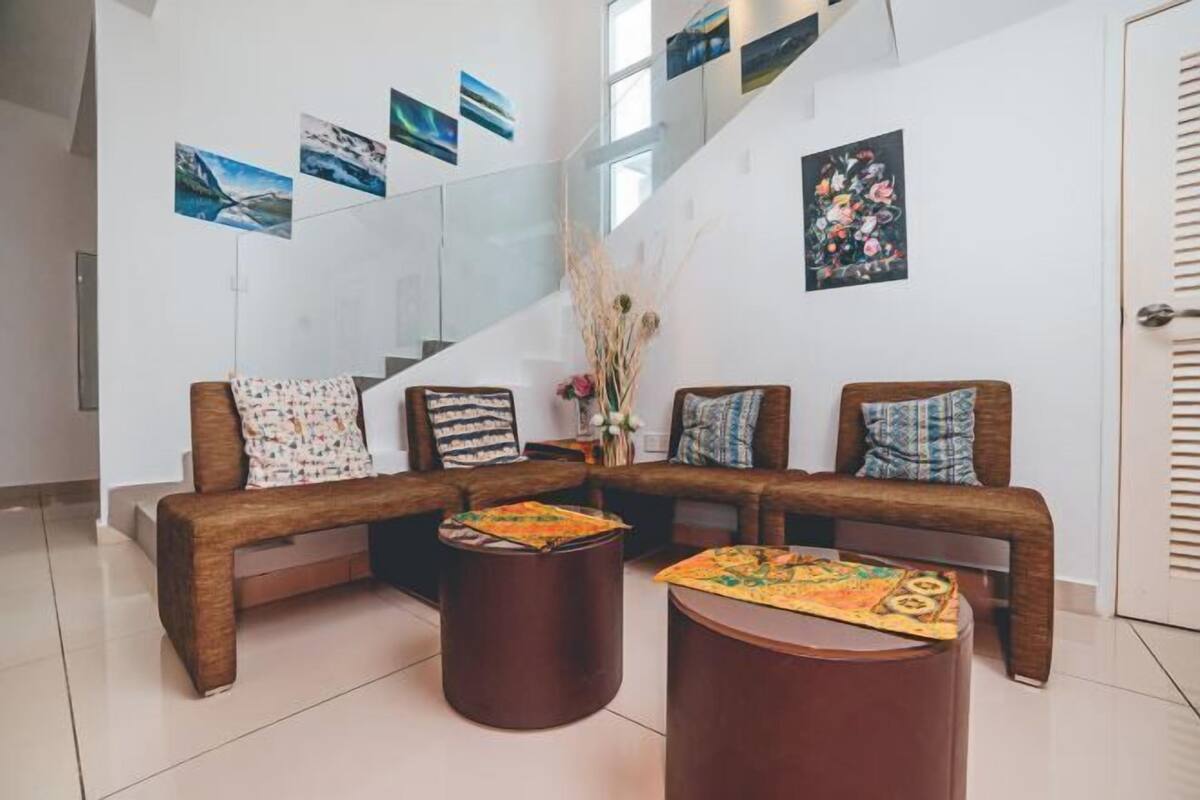 A modern living area with a sofa set, two round wooden tables, and a staircase with a glass railing.