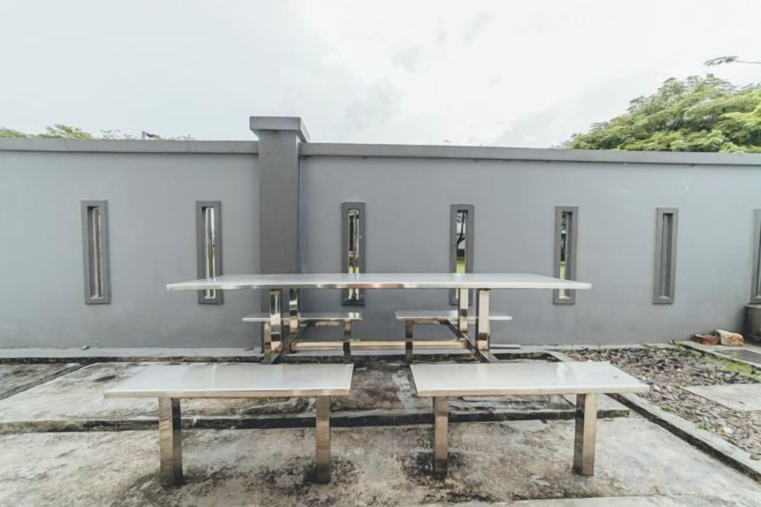 Terraço no telhado com mesa e bancos de metal, parede cinza com janelas, e céu nublado.