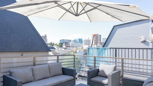 A rooftop terrace with a sofa set, a large umbrella, and a city view.