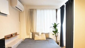 A hotel room with a bed, a bedside table, a plant, and a window with curtains.