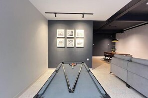 Une table de billard dans une pièce avec un mur gris et une collection de tableaux encadrés.