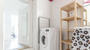 A laundry area with a washing machine, a drying rack, and a wooden shelf unit. - Charming 3BR Urban Retreat Vienna (Vienna)