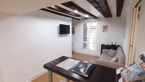 A room with a wooden ceiling, a white wall, a black table with papers, a white sofa, and a window with blinds. - OLD TOWN NEAR THE BEACH by www.sansebastianapartments.es (San Sebastian)