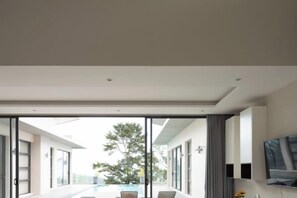 A modern interior with a large sliding glass door leading to an outdoor area, a flat-screen TV mounted on the wall, and a minimalist design. - THE PURE BANGPOR (Koh Samui)