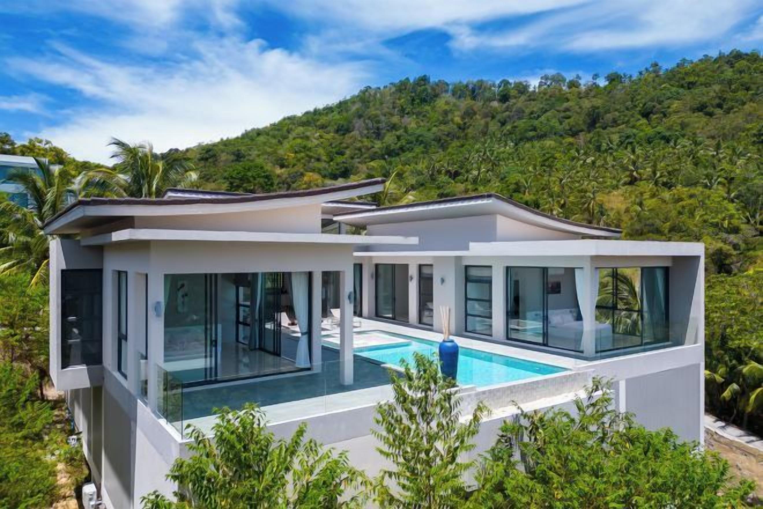 A modern house with a glass-enclosed swimming pool, surrounded by lush greenery and hills.