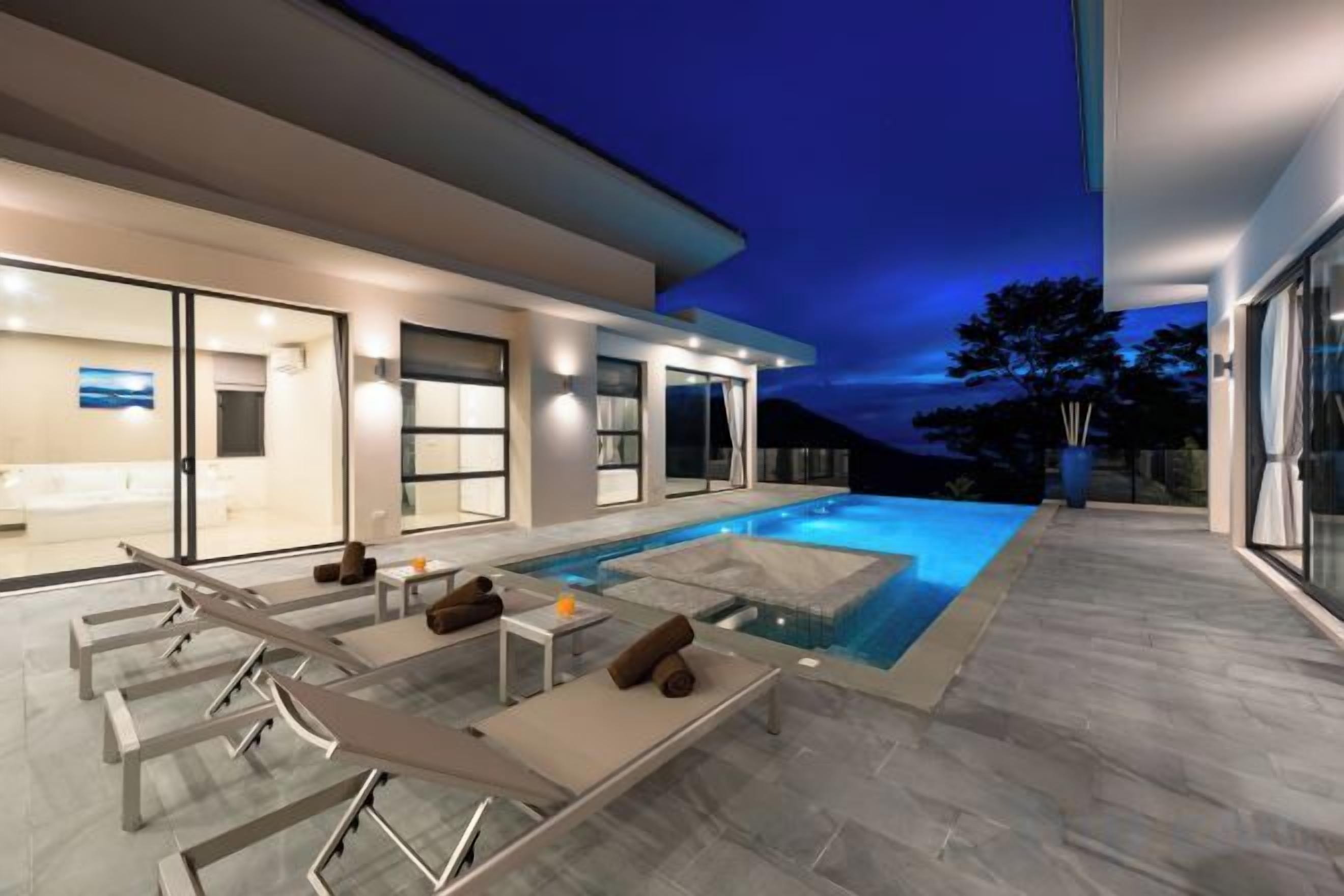 Una casa moderna con piscina, mobiliario exterior e interior bien iluminado.