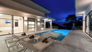 A modern house with a swimming pool, outdoor seating, and a well-lit interior.