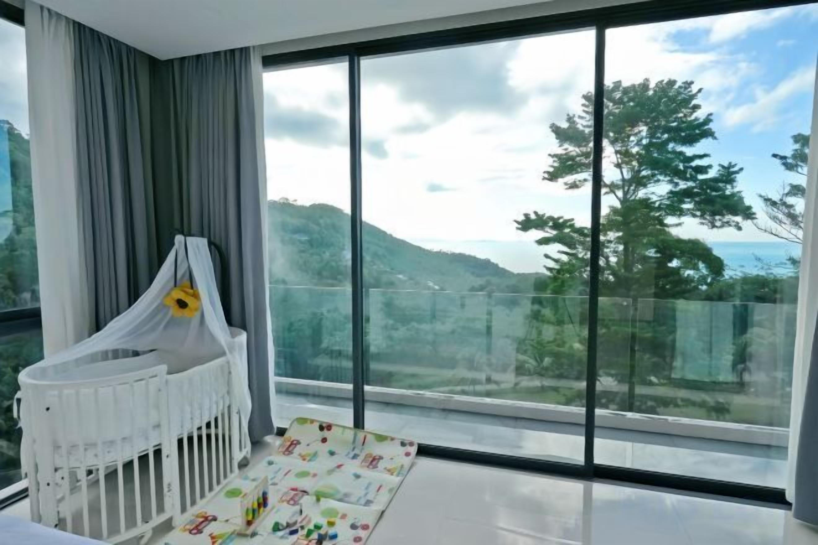 A room with a crib, a large window, and a view of a hilly landscape.