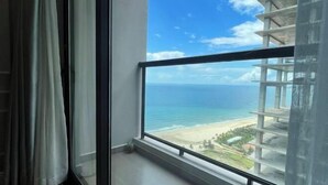 A room with a large window overlooking a beach and a building under construction. - Luxury Ocean View Suites_My Khe Beach_Hinata Apartment (Da Nang)