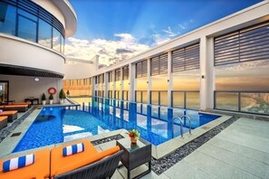 Una piscina en la azotea con vistas al horizonte de la ciudad, sillas de descanso y un comedor.