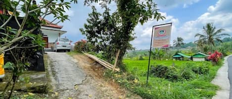 A rural road with a signboard, a parked car, and greenery.