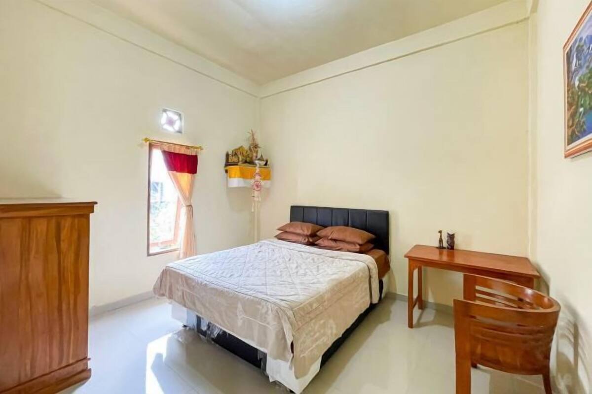 Een slaapkamer met een bed, een houten bureau, een stoel, een kledingkast en een raam met gordijnen.