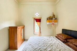 A bedroom with a bed, a wooden wardrobe, a window with curtains, and a wall-mounted shelf with decorative items.