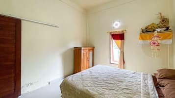 A bedroom with a bed, a wooden wardrobe, a window with curtains, and a wall-mounted shelf with decorative items.