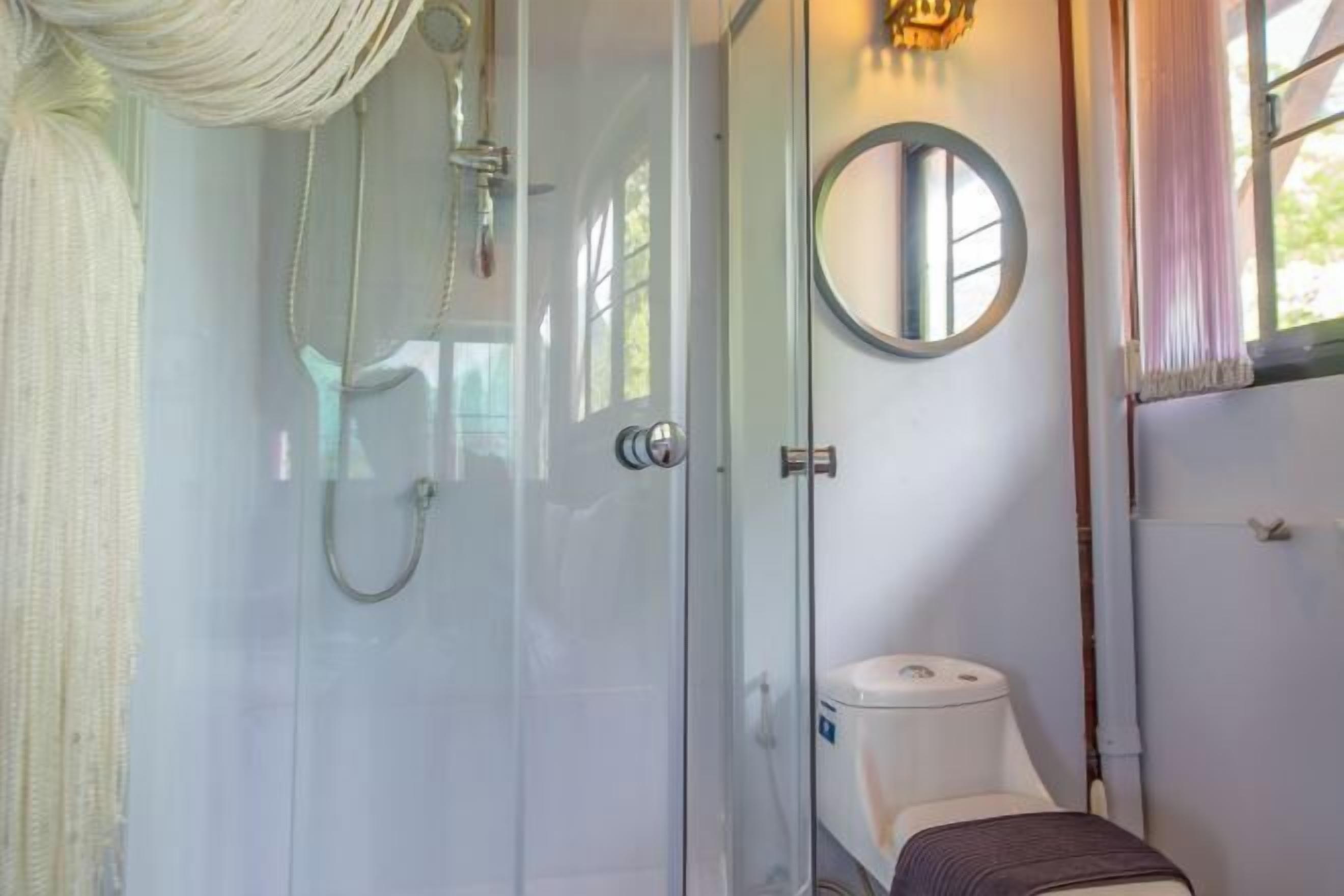 A bathroom with a glass shower enclosure, a toilet, and a round mirror.