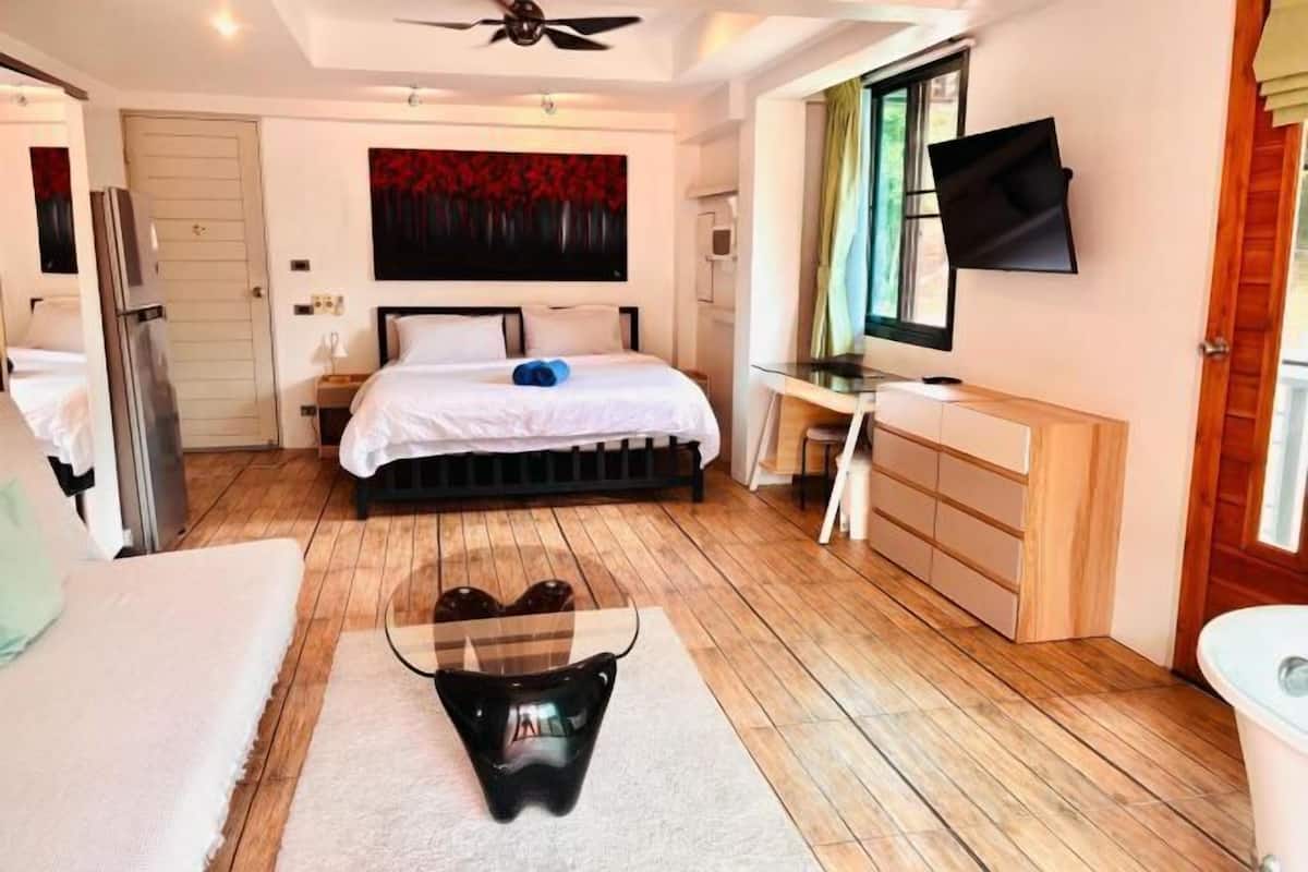 A bedroom with a bed, a desk, a TV, and a window.
