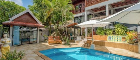 Un espace piscine agrémenté d’une statue, d’une terrasse en bois et d’un bâtiment à deux étages doté de balcons.