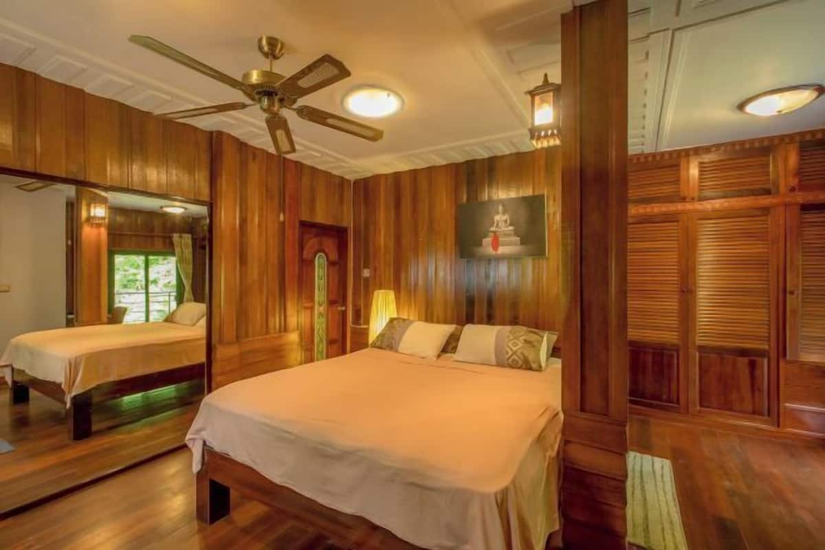 A room with a large bed, a ceiling fan, wooden paneling, and a mirror.