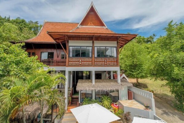 A two-story wooden house with a balcony, surrounded by lush greenery. - Penthouse Crystal Bay Apartments (Koh Samui)