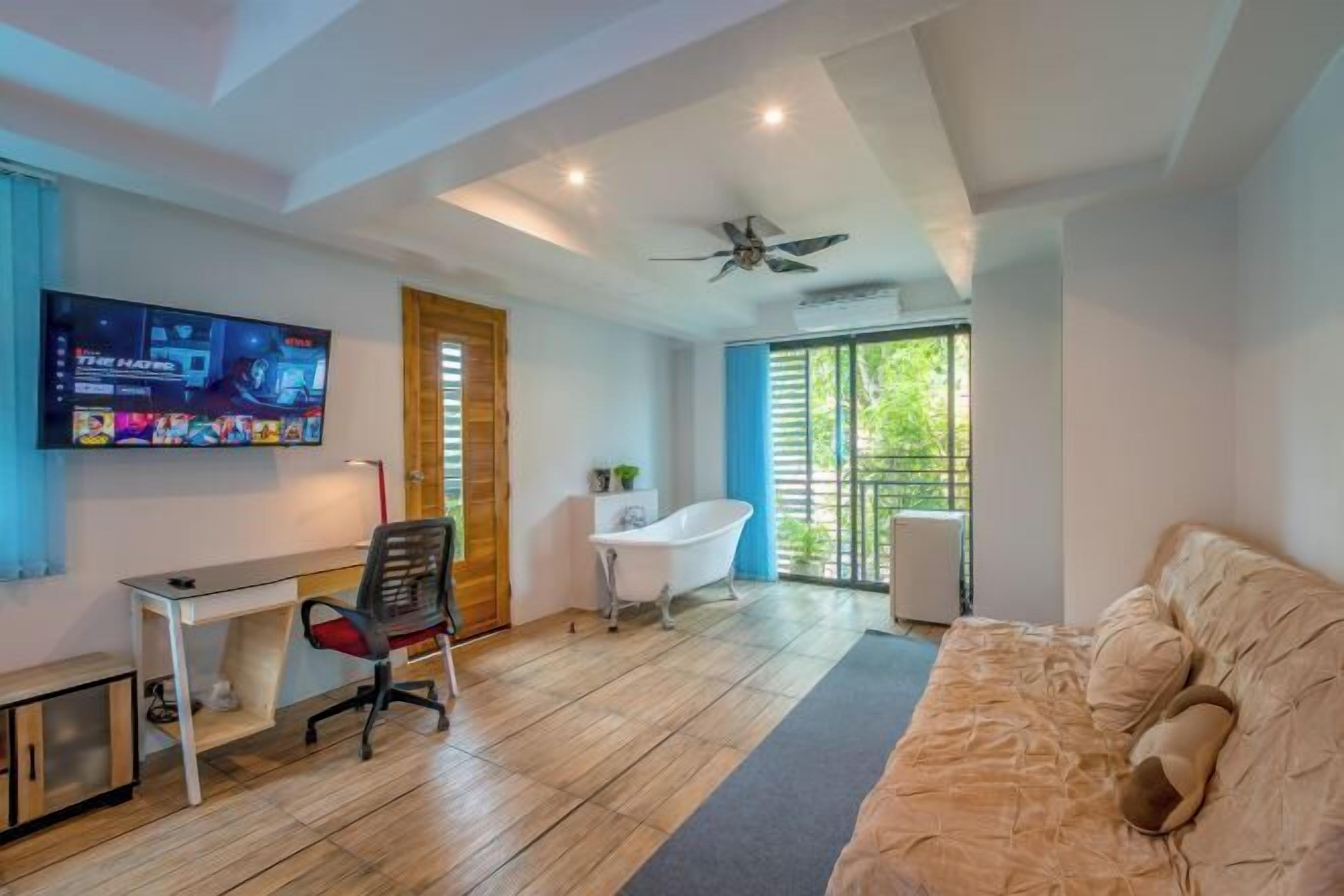A modern room with a desk, chair, bathtub, and a large window.