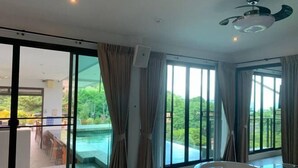 A modern bathroom with a large bathtub, large windows, and a view of a pool. - Penthouse Crystal Bay Apartments (Koh Samui)