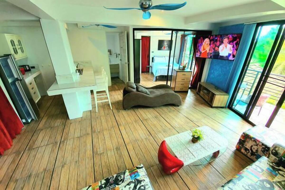 A modern living area with a sofa, a coffee table, and a TV. There is a kitchen area with a refrigerator and a microwave.