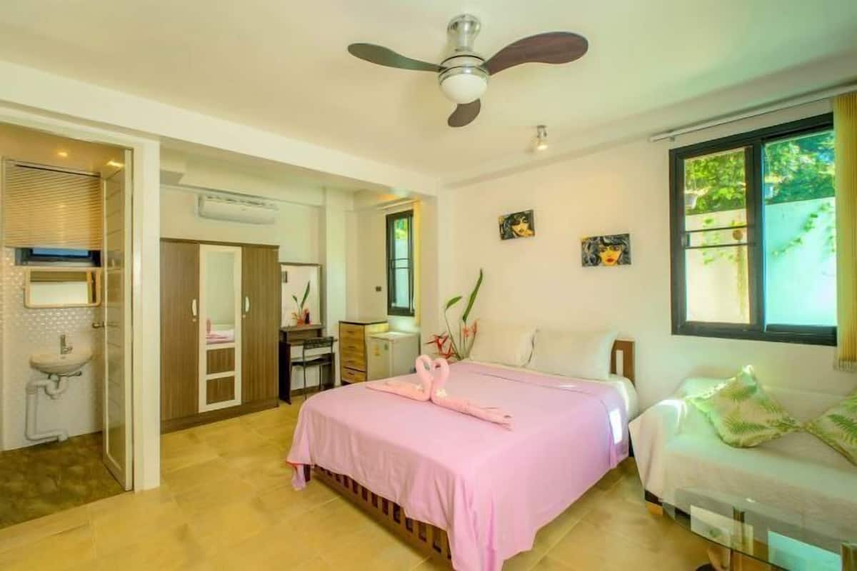 A bedroom with a bed, a ceiling fan, a window with a view, and a bathroom with a sink and mirror.