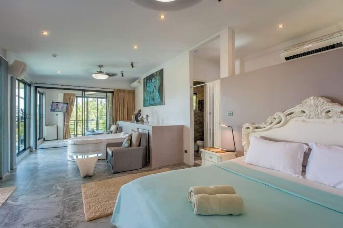 A bedroom with a large bed, a desk, and a chair, with a view of the outdoors.