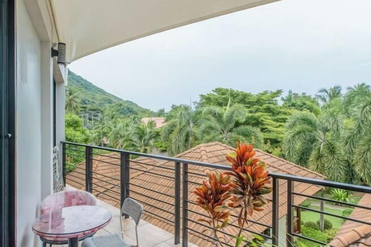 A balcony with a view of a lush green landscape and a thatched-roof structure.