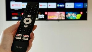 A hand holding a Haier remote control in front of a TV displaying various streaming services. - Sman Resort (Koh Samui)