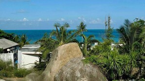 A coastal view with a large rock in the foreground, palm trees, and a clear blue sky. - Sman Resort (Koh Samui)