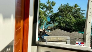 A view through a window with a view of a building and trees. - Sman Resort (Koh Samui)