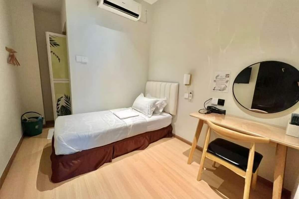 Een kleine, schone kamer met een bed, een bureau, een stoel, een airconditioning en een spiegel.