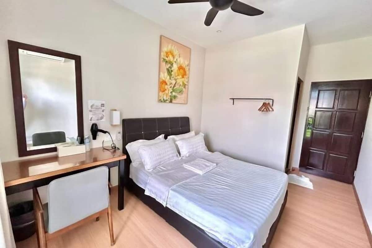 Een slaapkamer met een bed, bureau, stoel en plafondventilator.