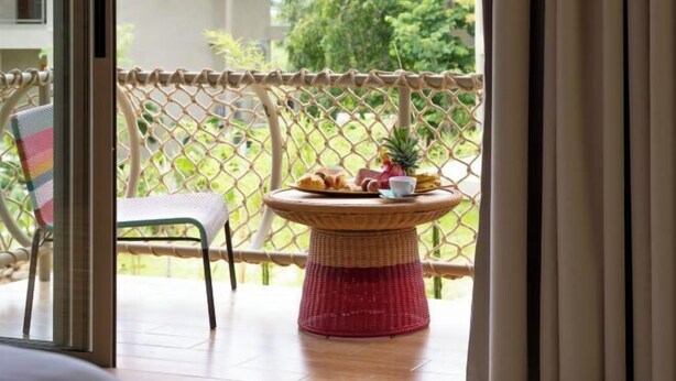 A balcony with a wicker table, a chair, and a view of greenery. - Carbana Lodge, 1 Bedroom - Eco Lodge, Koh Samui (Koh Samui)