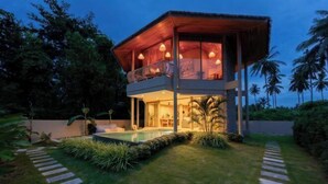 Een tweelaags huis met een zwembad, omgeven door een verzorgde tuin en palmbomen.