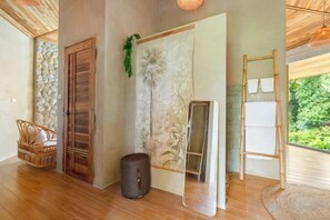 A room with a wooden floor, a door, a wall with a decorative panel, a small stool, and a ladder leaning against the wall. - Carbana Lodge, 1 Bedroom - Eco Lodge, Koh Samui (Koh Samui)