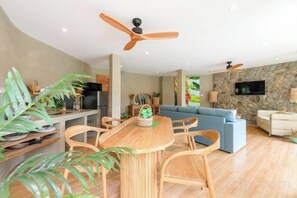 A modern living room with a wooden dining table, blue sofa, and a stone accent wall. - Carbana Lodge, 1 Bedroom - Eco Lodge, Koh Samui (Koh Samui)