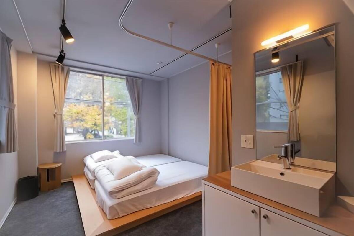 Una habitación de hotel moderna con cama, mesita de noche, espejo y ventana con cortinas.