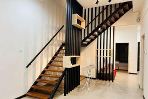 A modern staircase with wooden steps and black railings, leading to a living area with a sofa and a TV.