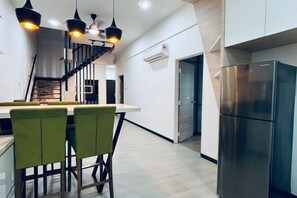 Una cuina moderna amb un frigorífic d'acer inoxidable, una zona de menjador amb caires verds i una escala que condueix a un altre pis.