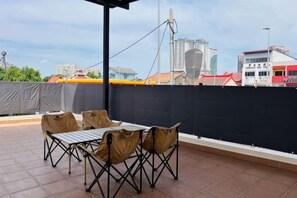 A rooftop patio with a table and chairs, a black privacy screen, and a cityscape view.
