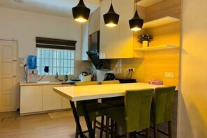 A modern kitchen with a central island, pendant lighting, and a window with blinds.