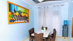A dining area with a table and chairs, a painting on the wall, and a water dispenser.